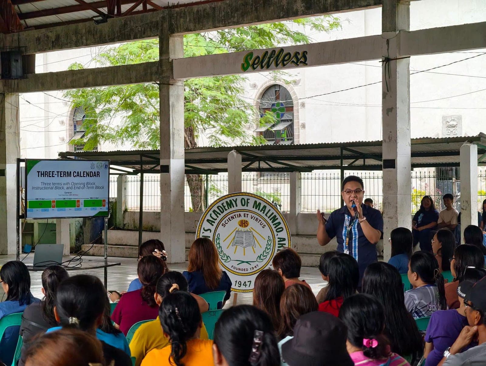 A teacher presents the school's three-term calendar on screen beside the St. Joseph's Academy seal